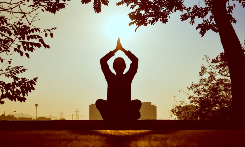 Silhouette of a person practicing yoga outdoors during sunrise, creating a calming atmosphere.