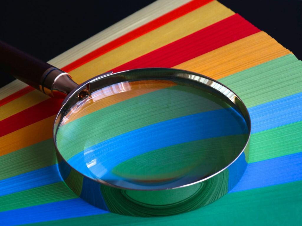 Magnifying glass resting on vibrant rainbow-colored paper close-up.