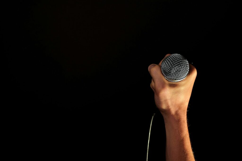 Close-up of a hand firmly gripping a microphone against a dark backdrop.